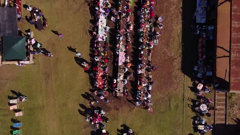 vista aérea de personas comiendo al aire libre en largas mesas de picnic