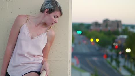 chica rubia de pelo corto con raíces oscuras que se ve feliz, luego se asoma por el borde de un edificio alto hacia la calle de la ciudad al atardecer, luego vuelve a la cámara