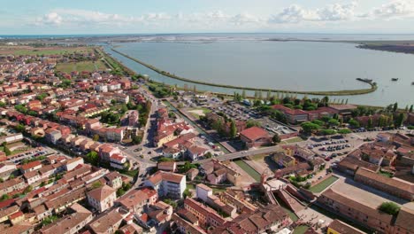 Comacchio,-Italy,-drone-orbit-view-of-urban-infrastructure,-city's-canal-and-The-Valli-di-Comacchio-lagoon