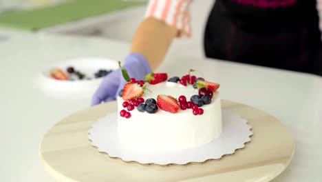 the girl, the chief confectioner, decorates forest berries, strawberries, a homemade cake