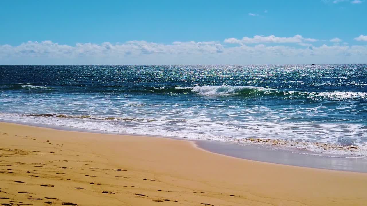 HD Hawaï Kauai, ralenti, plan large statique en contre-jour de vagues océaniques étincelantes déferlant sur la plage, avec un bateau dans le coin droit du cadre se dirigeant de droite à gauche vers le centre, et des nuages à l'horizon