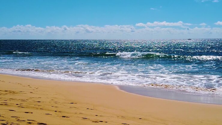HD Hawaï Kauai, ralenti, plan large statique en contre-jour de vagues océaniques étincelantes déferlant sur la plage, avec un bateau dans le coin droit du cadre se dirigeant de droite à gauche vers le centre, et des nuages à l'horizon