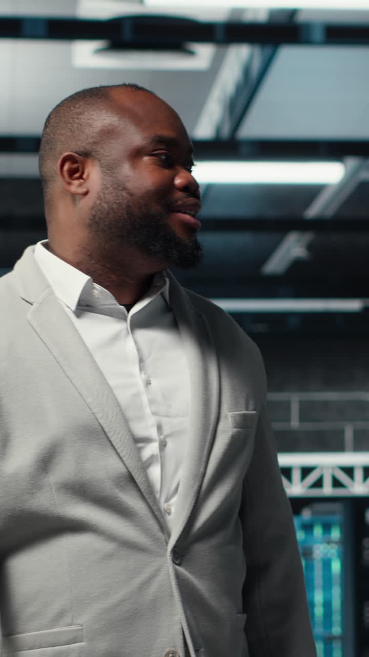 Vertical video Smiling engineer walking in data center, checking hardware for system stability