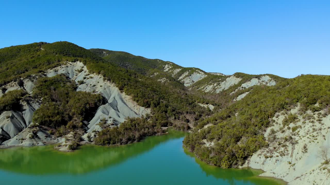 Lake on high mountains with green vegetation of sharp slopes reflecting on calm water surface, bright blue sky