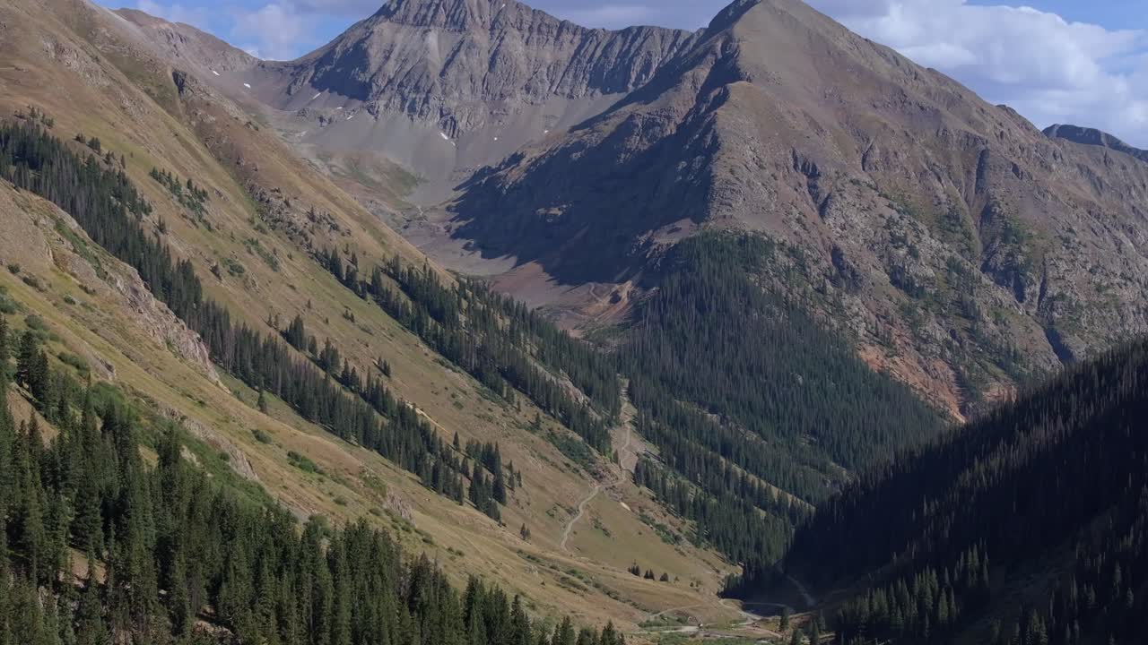 Veicolo parcheggiato a lato di una strada di montagna con vista su una vasta valle alpina, sorvolo aereo.