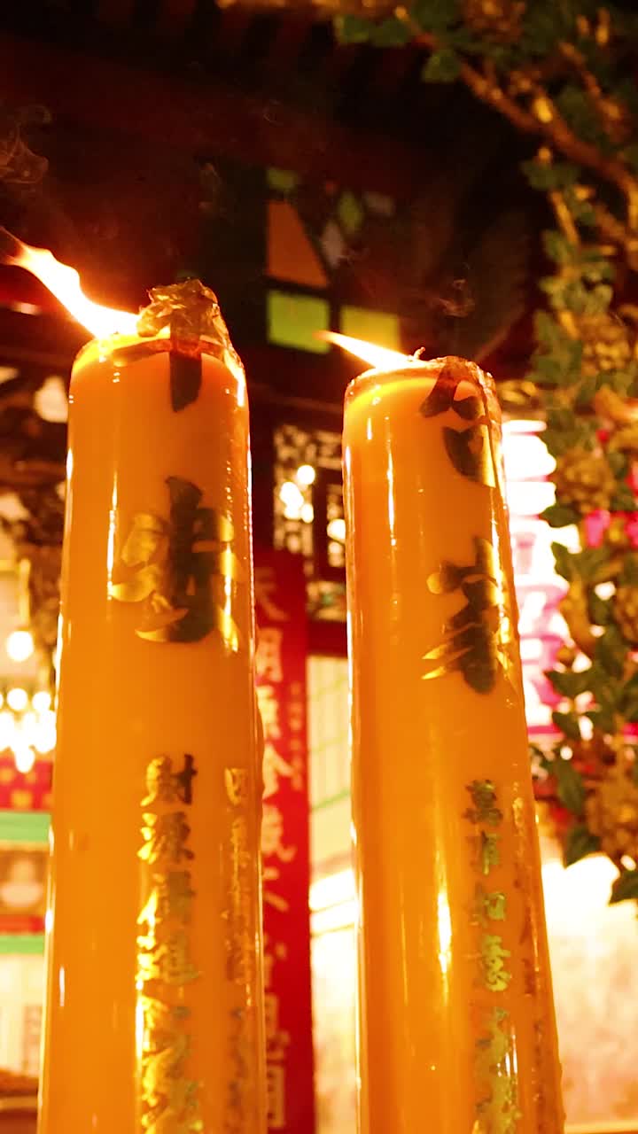 Tall yellow candles with gold inscriptions burn brightly inside a traditional Chinese temple at night