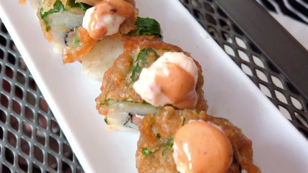 Close-up of gourmet sushi with crispy topping and orange sauce on a plate.