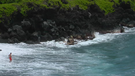 Un-Hombre-Lucha-Contra-Un-Gran-Oleaje-En-Una-Playa-De-Arena-Negra-En-Hawaii