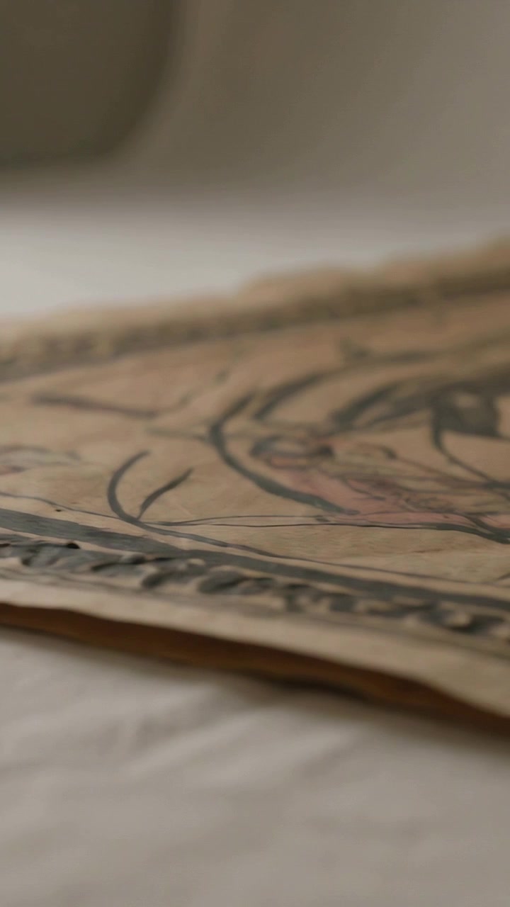 Video verticale: La telecamera inizia a scansionare della carta decorata su un tavolo, rivelando linee inchiostrate e una piega.