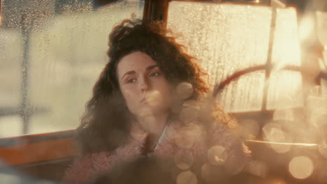 young pensive woman in warmly lit car with rain-streaked windows