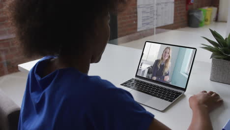 vista posterior de una mujer afroamericana haciendo una videollamada con una colega en una computadora portátil en la oficina