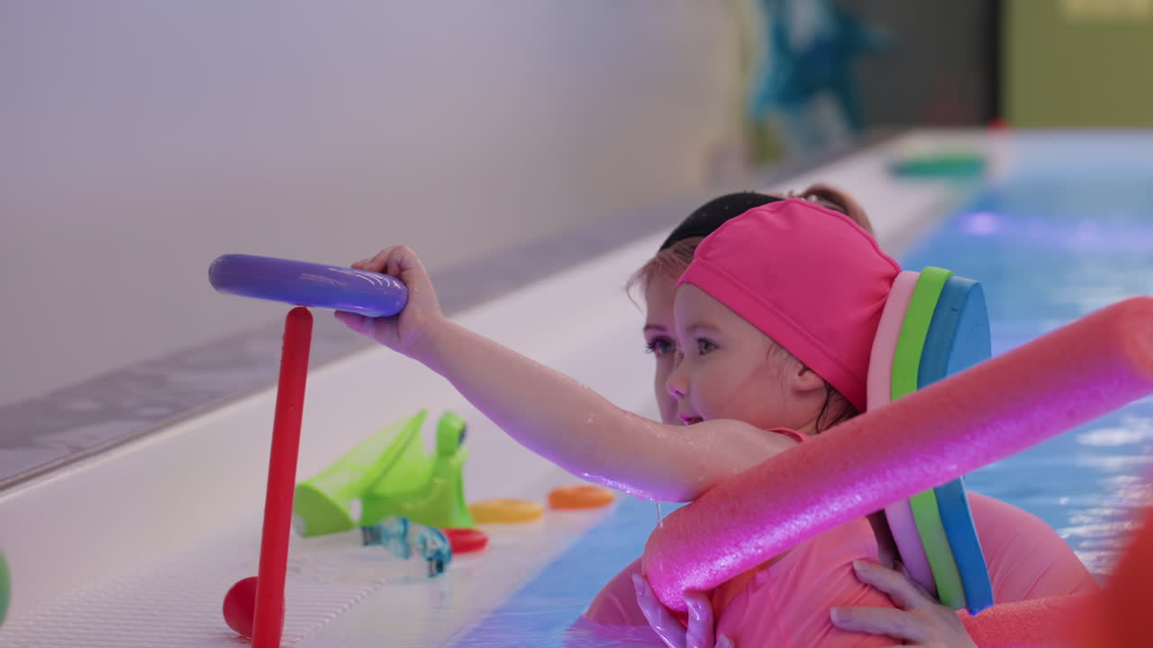 Baby stacking donut toys into pyramid shape on table, tiny hands sorting colors, focused gaze, patient learning, gentle guidance nearby, bright light, tidy arrangement in close indoor scene
