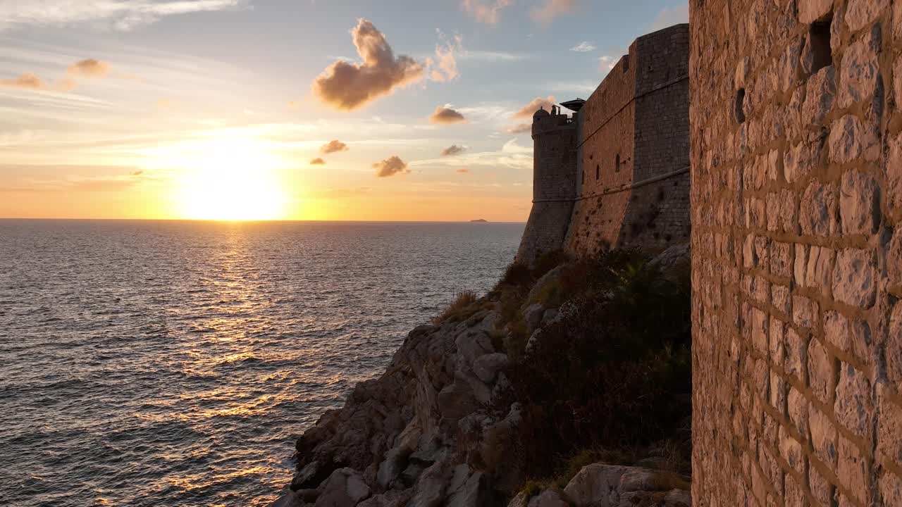 Aerial pedestal shot descending next to the city walls of Dubrovnik, Croatia looking out to the sun setting into the sea.