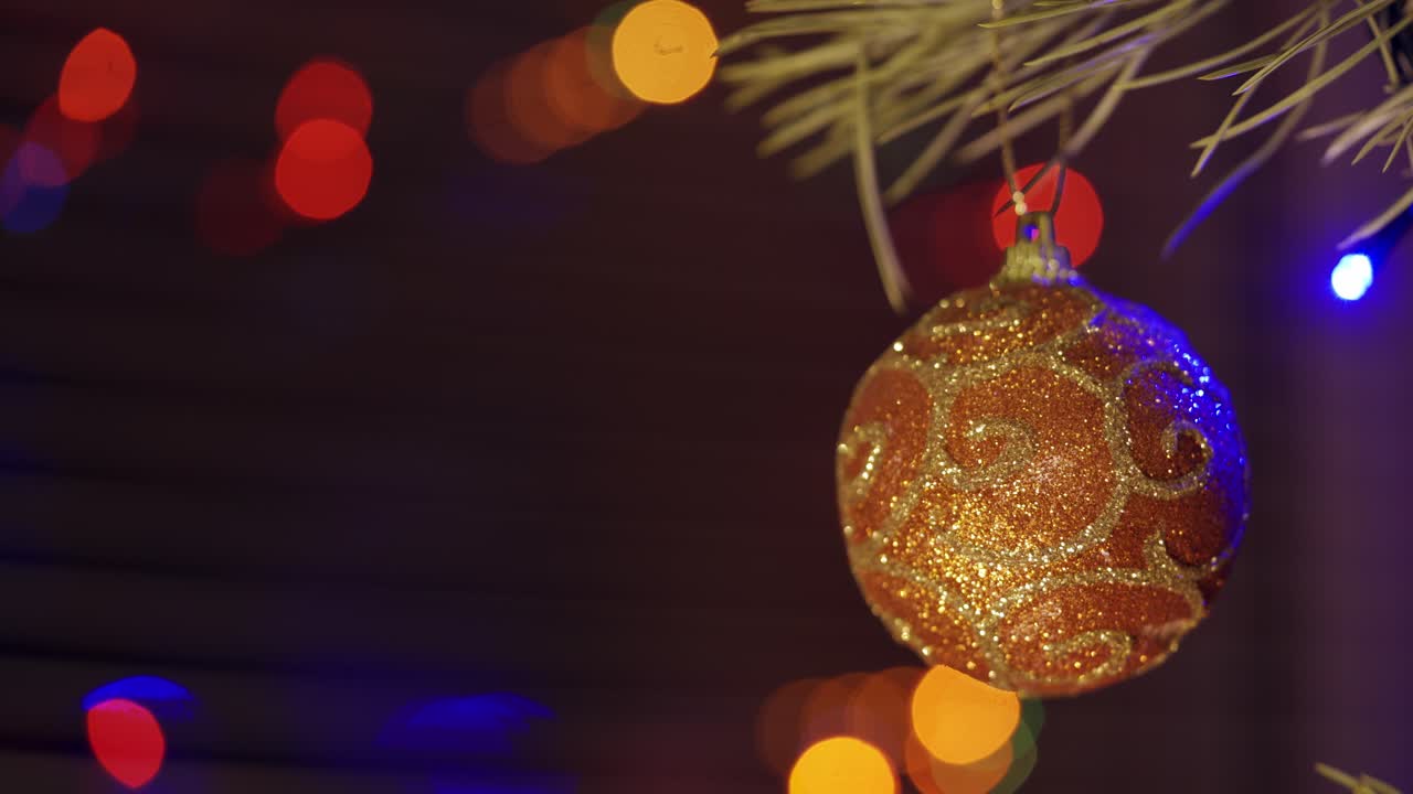 New Year's toy swinging on a branch. Beautiful brown Christmas ball with white pattern on abstract blurred holiday background. Blinking garland on a Christmas bauble indoors.