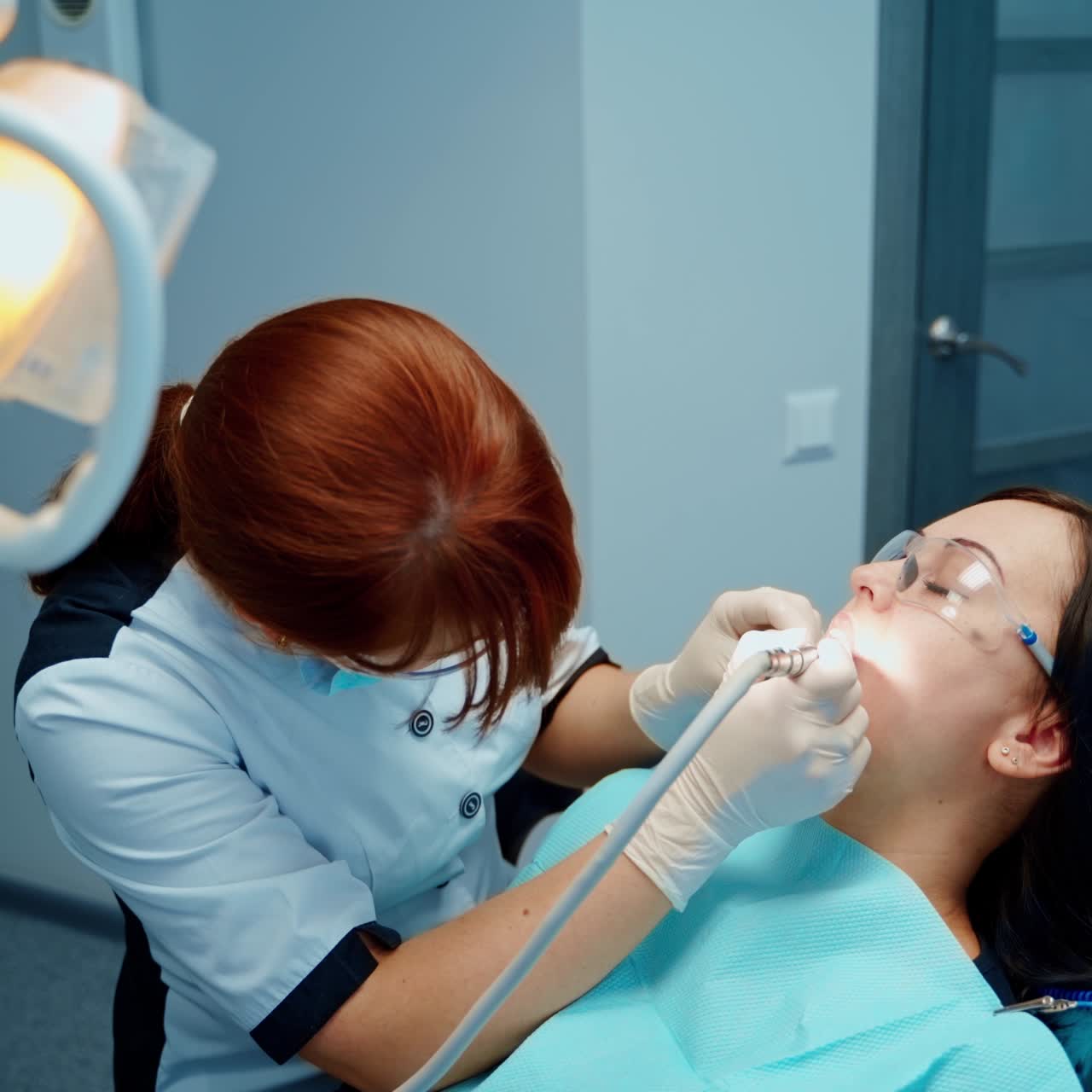 Medical procedure in dentistry. Young woman in protective glasses in dental chair. Female stomatologist cures patient's teeth in clinic.
