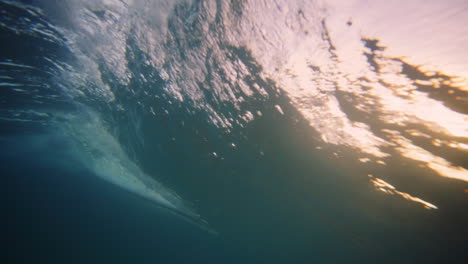 Underwater-ocean-wave-breaking-and-glowing-from-sunlight-as-surfer-rides