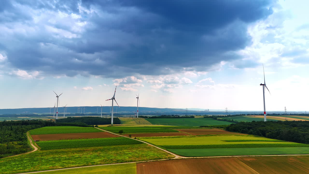Footage over the agricultural fields with multiple wind turbines. Grey cloudscape in the sky above