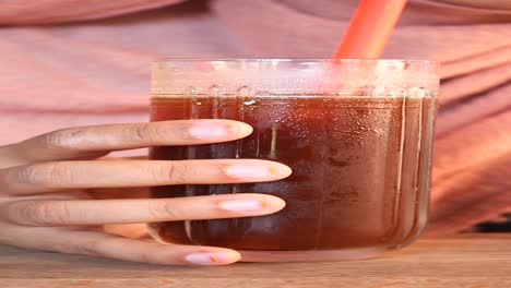 close-up of a hand holding a glass of iced tea with a red straw