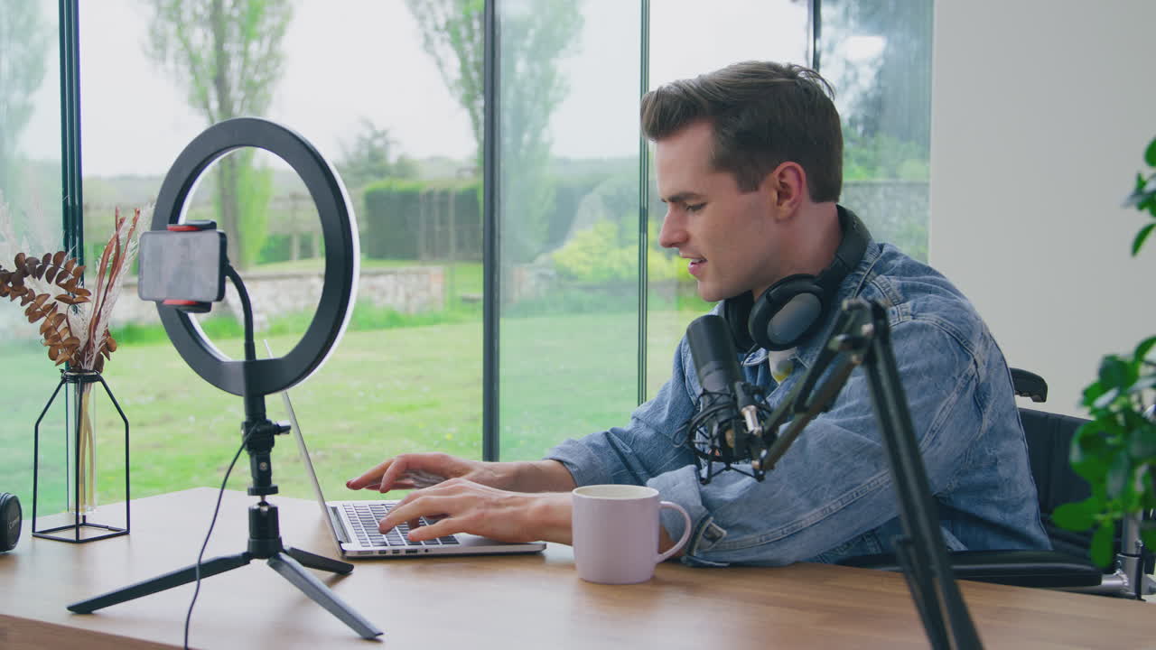 Vlogger uomo con cuffie e microfono che digita sul laptop prima della diretta streaming.
