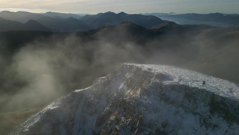 hiker reaching summit of snowy mountain with clouds swirling stob ban highlands scotland