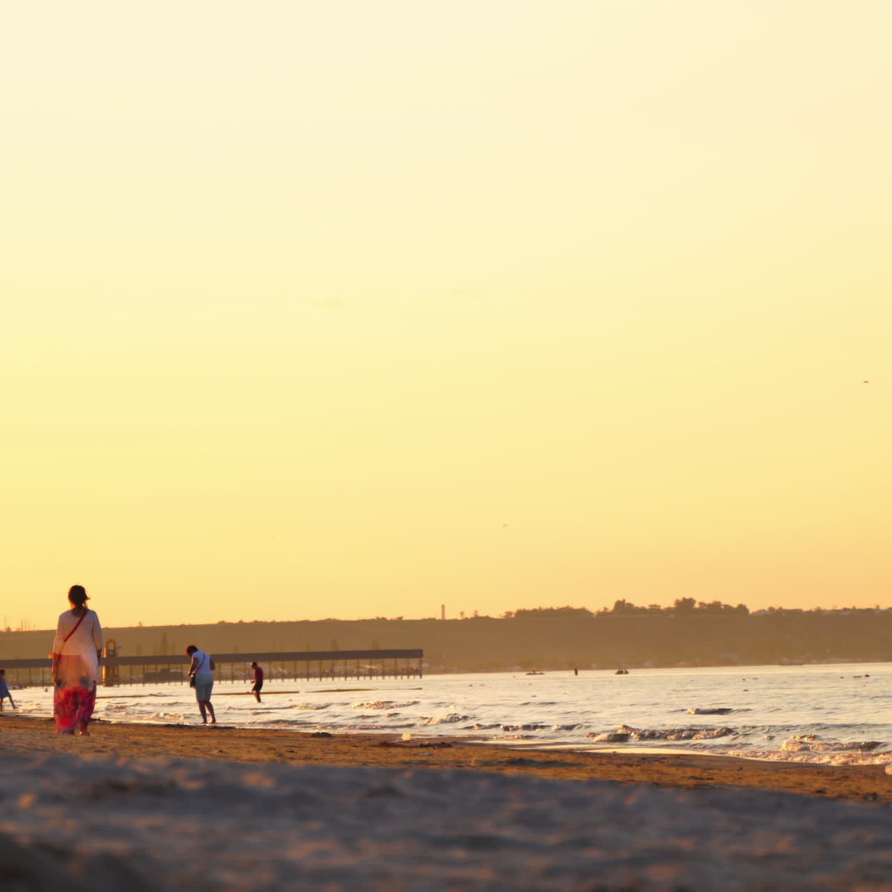 People walking along the sea shore at sunset. Evening background of the seaside and many people enjoying the time near water in summer.