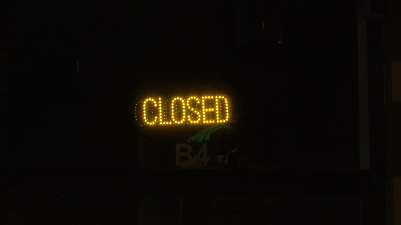 Insegna LED gialla "CHIUSO" si illumina nella vetrina di un negozio dopo l'orario di chiusura, 4K.