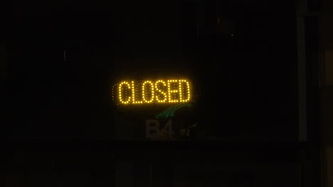 led yellow closed sign glows in business window after hours, 4k