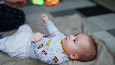 caucasian infant boy lies on the plaid and tosses little hands and legs. mom is holding a bright toy over the baby. close up.