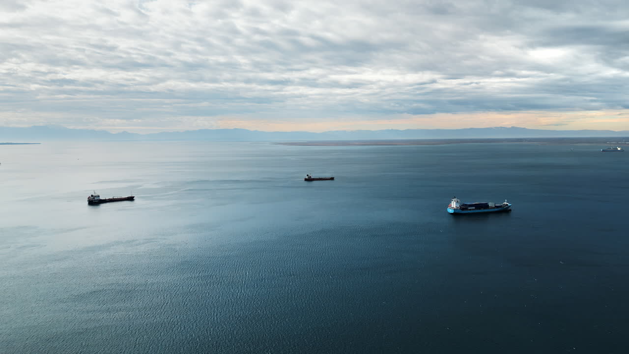 Aerial drone view of cargo ships floating in the middle of a large body of water. Clear sky, calm blue water