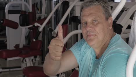 hombre mayor con el pulgar hacia arriba y sonríe entre los ejercicios en el gimnasio
