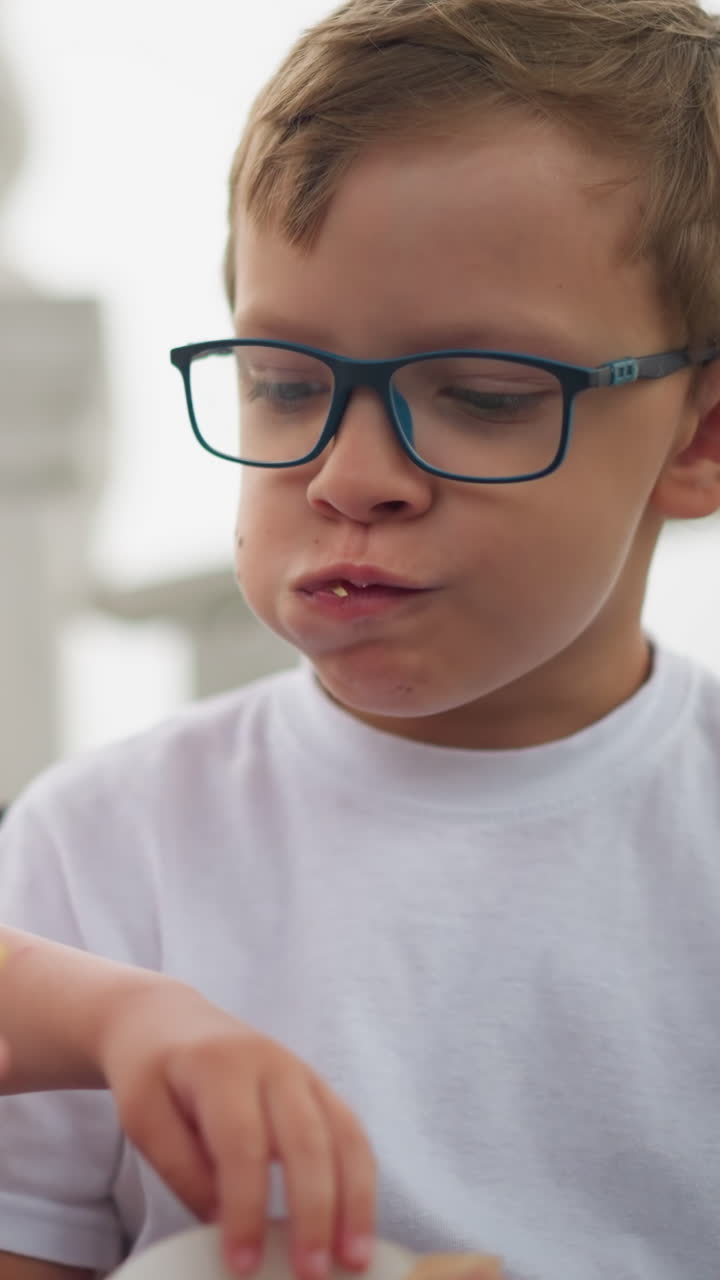 dos hermanos están sentados en un banco, compartiendo papas fritas, el niño menor tiene un bocadillo en su mano derecha mientras el hermano mayor le da a su hermano menor algunas papas fritas para disfrutar