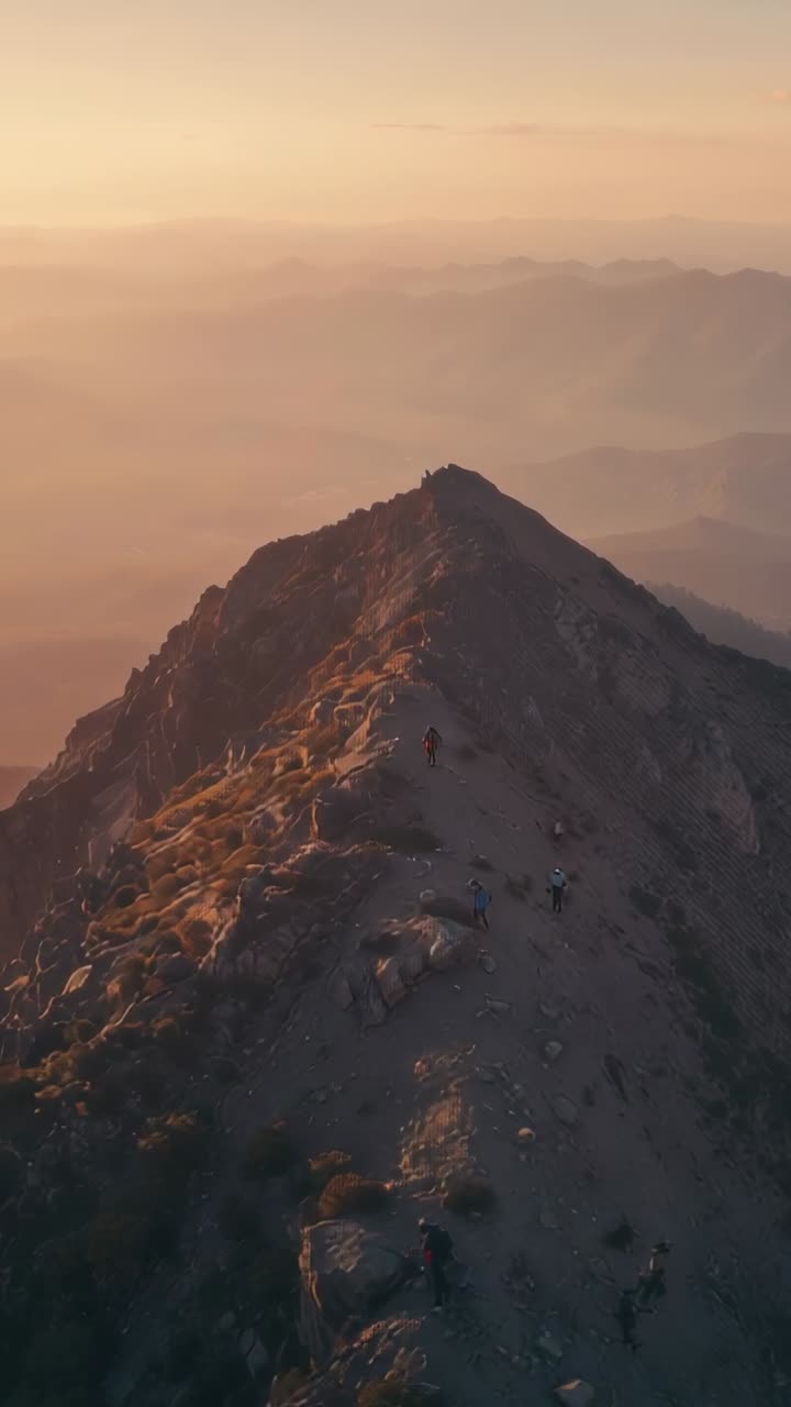 Vertical video: Drone pullback showing hiking group moving along ridge to summit with red jacket