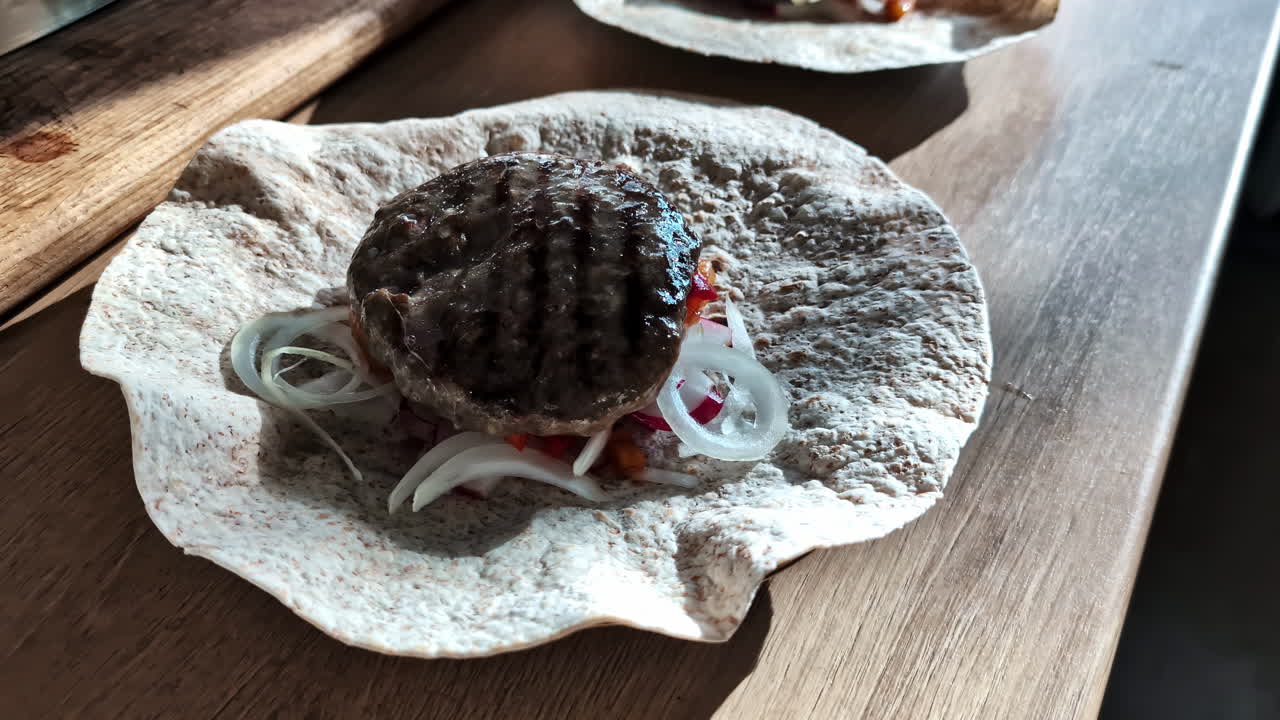 Closeup view of tortilla filled with colorful mixture of vegetables and adding of grilled meat on top.