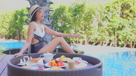 young woman chilling by pool with tray of treat, coffee, snack