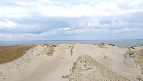 sandy dune of neringa while people walking on and reveal of curonian lagoon, ascending drone view