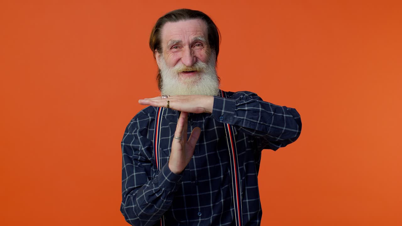 수염과 회색 머리카락을 가진 행복한 노인이 타임 아웃 손짓을 합니다.