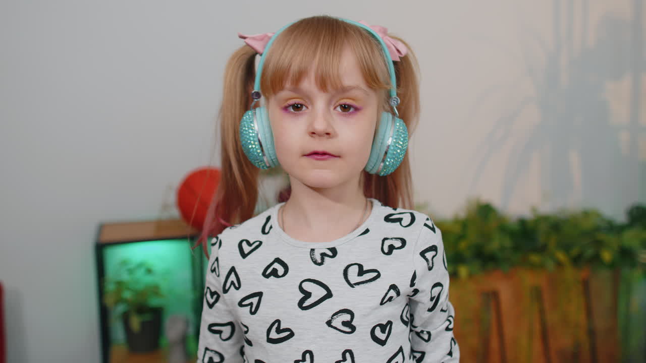 Bambina felice bambina con le cuffie che balla e salta mentre ascolta la musica a casa da sola