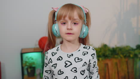 happy child girl kid in headphones dancing and jumping while listening to the music at home alone