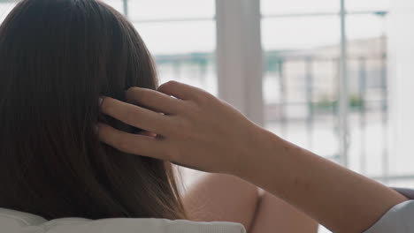 woman touches hair resting in armchair by large window