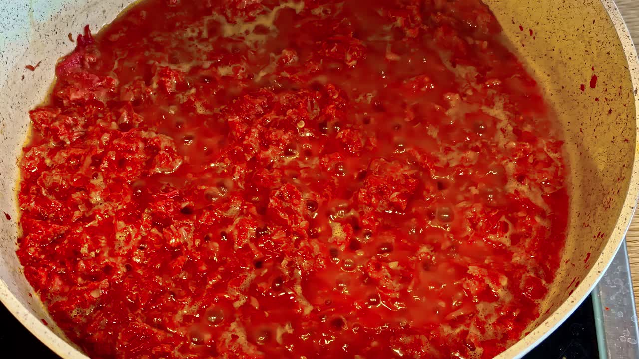 Primo piano di una pentola di salsa rossa che sobbolle con bolle visibili e ingredienti dalla consistenza