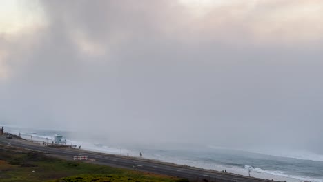 niebla rodando rápidamente durante una puesta de sol que cubre la costa y la carretera y la gente en la playa