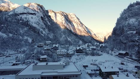 cold town dale in shadow during winter season - aerial over village and school with sun in mountain peak