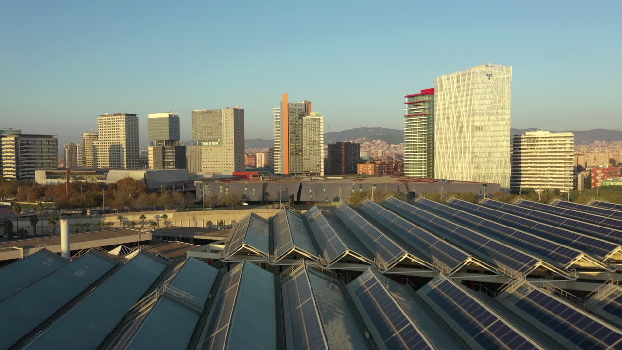 Drone voando sobre painéis solares no Parque Fórum de Barcelona com arranha-céus ao fundo.