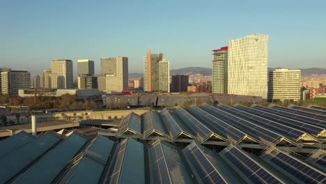 Drone-flying-over-solar-panels-at-forum-park-of-Barcelona-with-skyscrapers-in-background