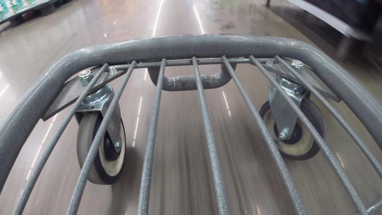Una vista a livello del suolo di un carrello della spesa che si muove in un grande magazzino illuminato a fluorescenza.