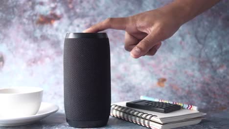 person using a black bluetooth speaker on a desk