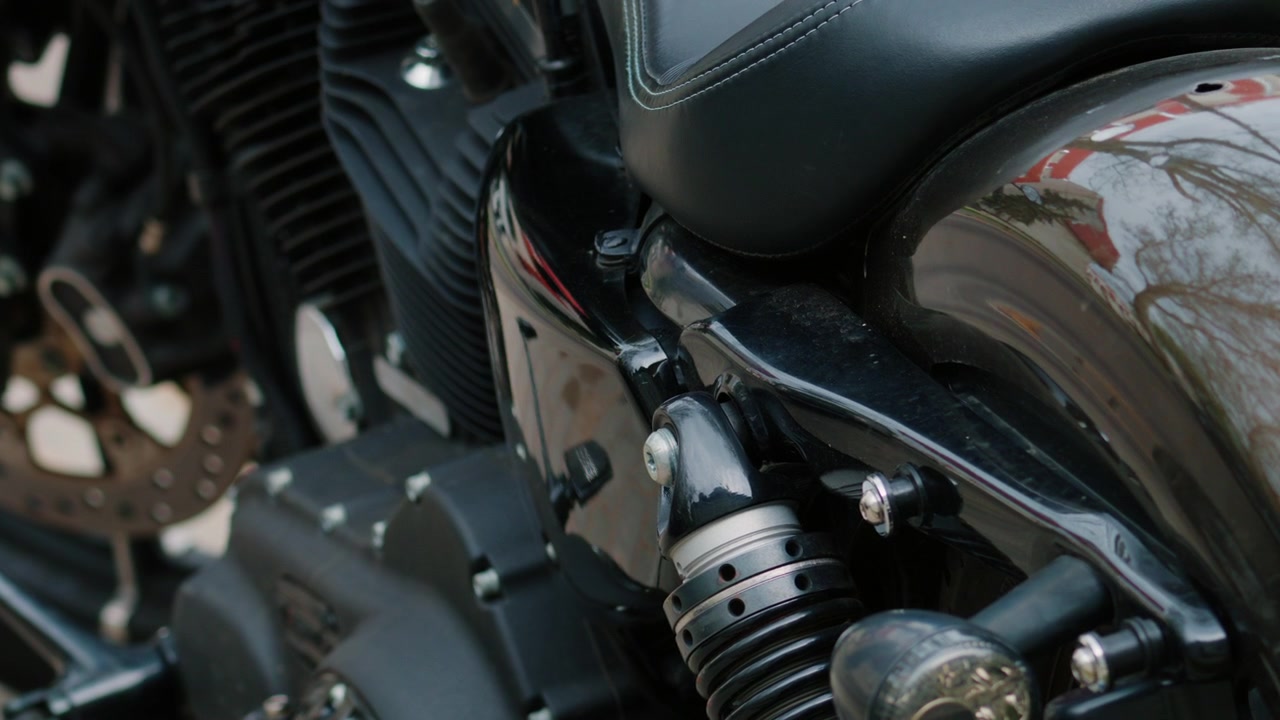 Siyah bir motosiklet motorunun, arka süspansiyonunun ve parlak gövde detaylarının yakın çekimi.
