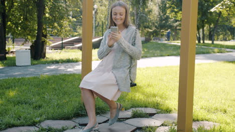woman using phone on a swing in a park