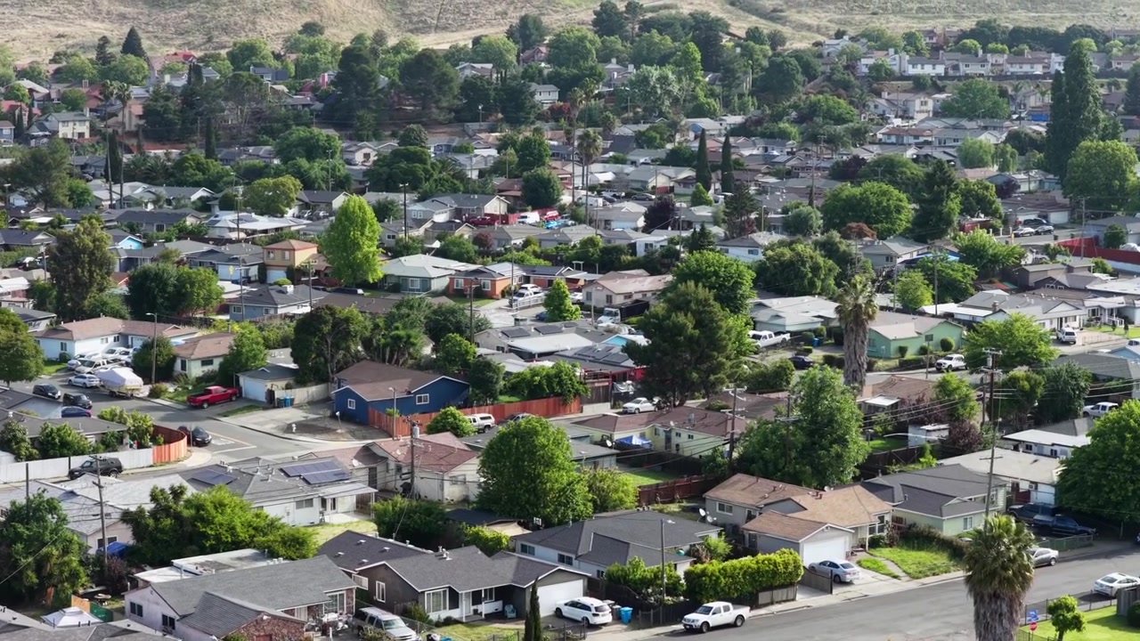 Quartiere residenziale di Vallejo con case unifamiliari, pannelli solari e palme che fiancheggiano le strade suburbane, dolci colline e l'espansione urbana che si estende fino all'orizzonte. California, USA. Ampia ripresa aerea.