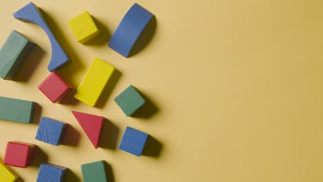 toma aérea de bloques de construcción de madera coloridos en un fondo de estudio amarillo